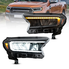 A pair of black aftermarket car headlight assemblies shown on a white background, with a faded orange pickup truck in the upper background. The headlights feature a bright white main light, an amber side marker light, and a horizontal amber LED daytime running light strip.